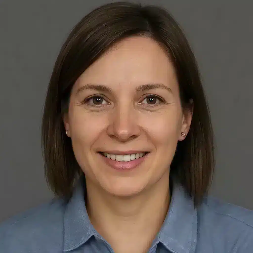 Porträt einer computergenerierten Frau mit glatten braunen Haaren und blauer Bluse vor grauem Hintergrund.